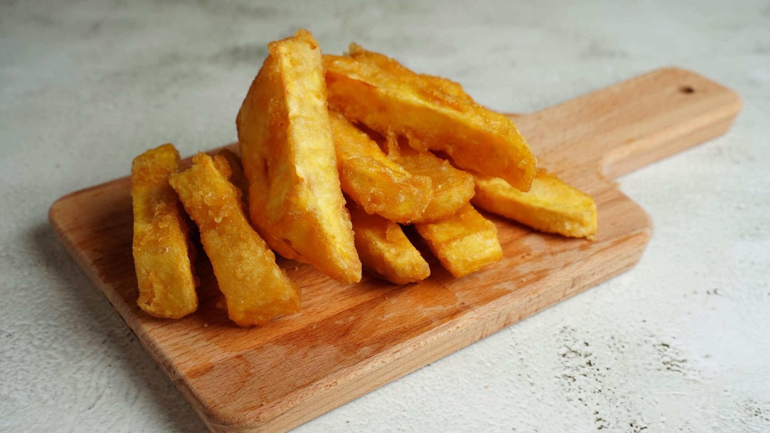 Thick-cut golden fried potato chips on a wooden serving board.