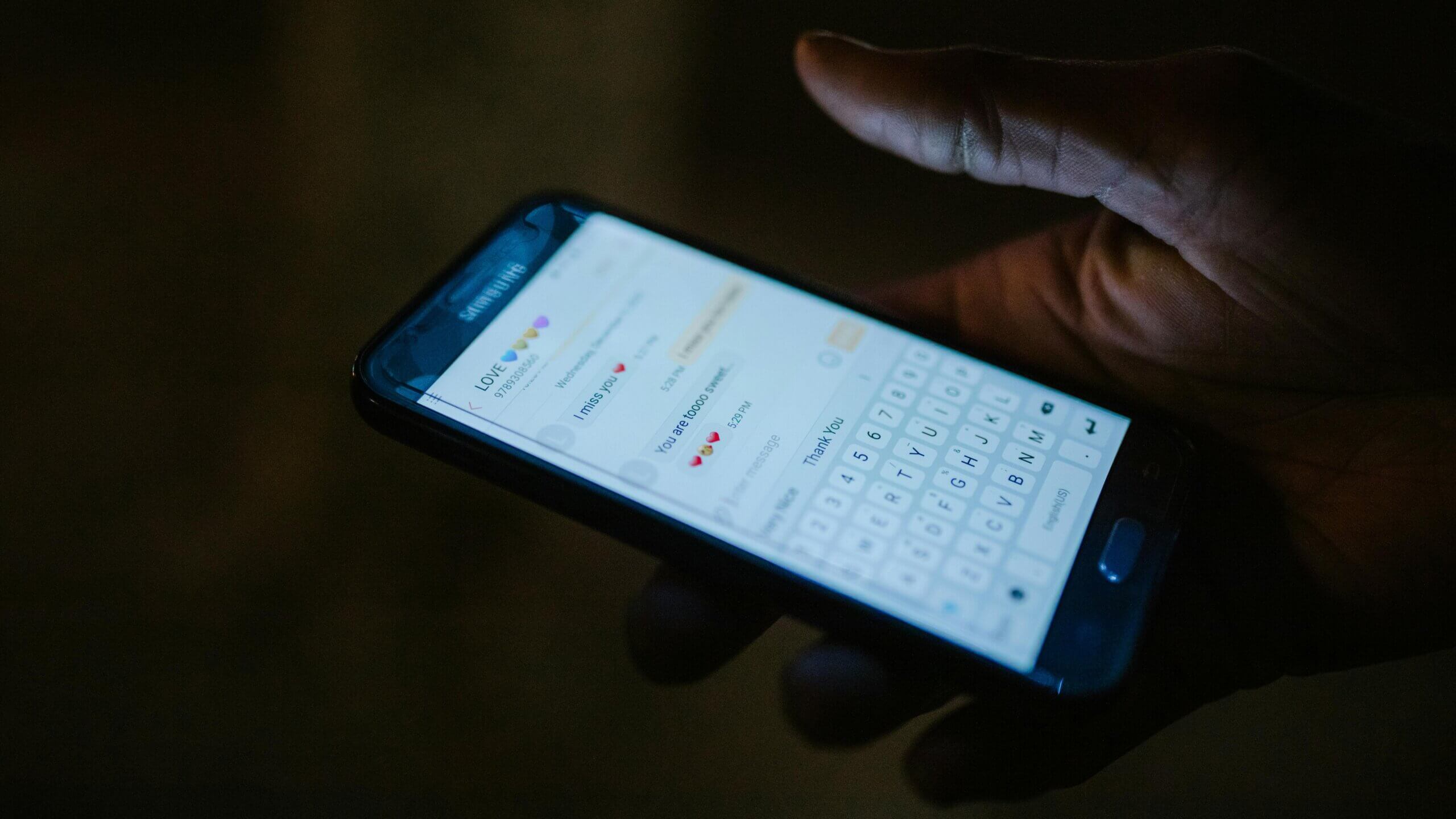 Hand holding Samsung smartphone displaying a text conversation with messages expressing love and missing each other.