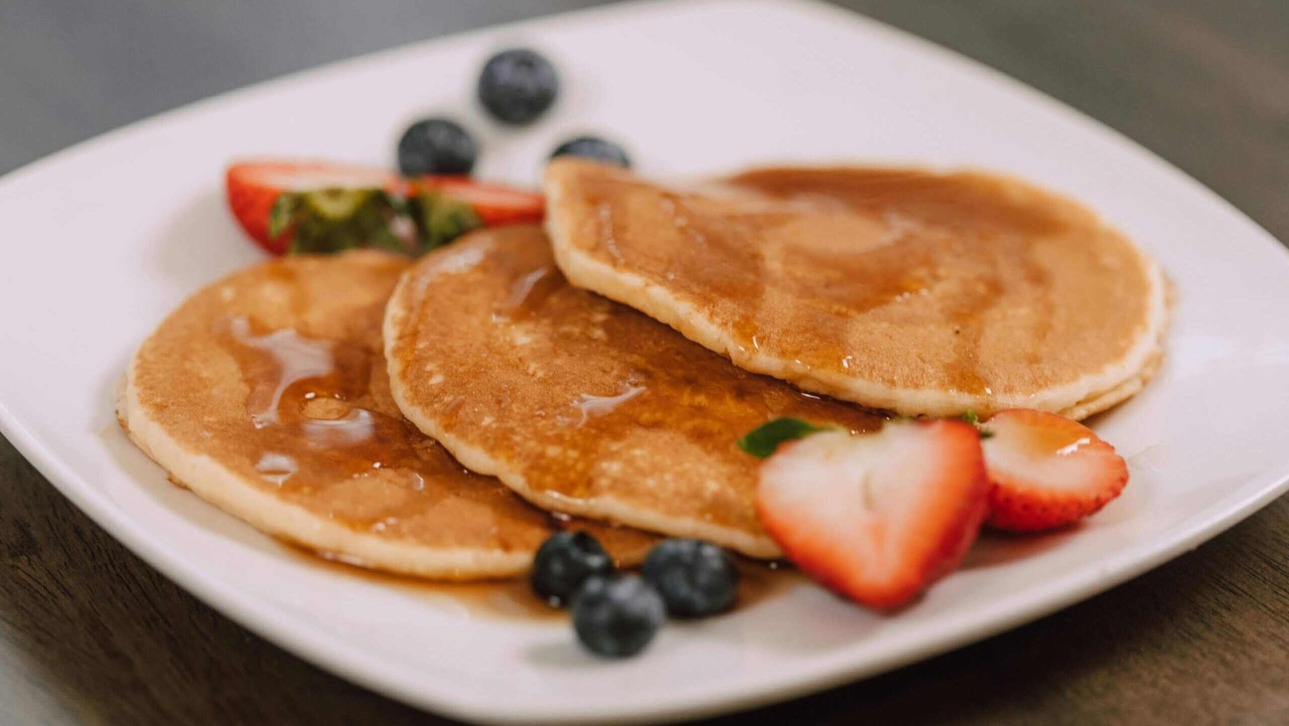 Three pancakes with syrup, strawberries, and blueberries on a white plate