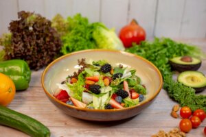 Mixed green salad with strawberries, blackberries, blueberries, and almonds in a bowl surrounded by fresh vegetables and fruits