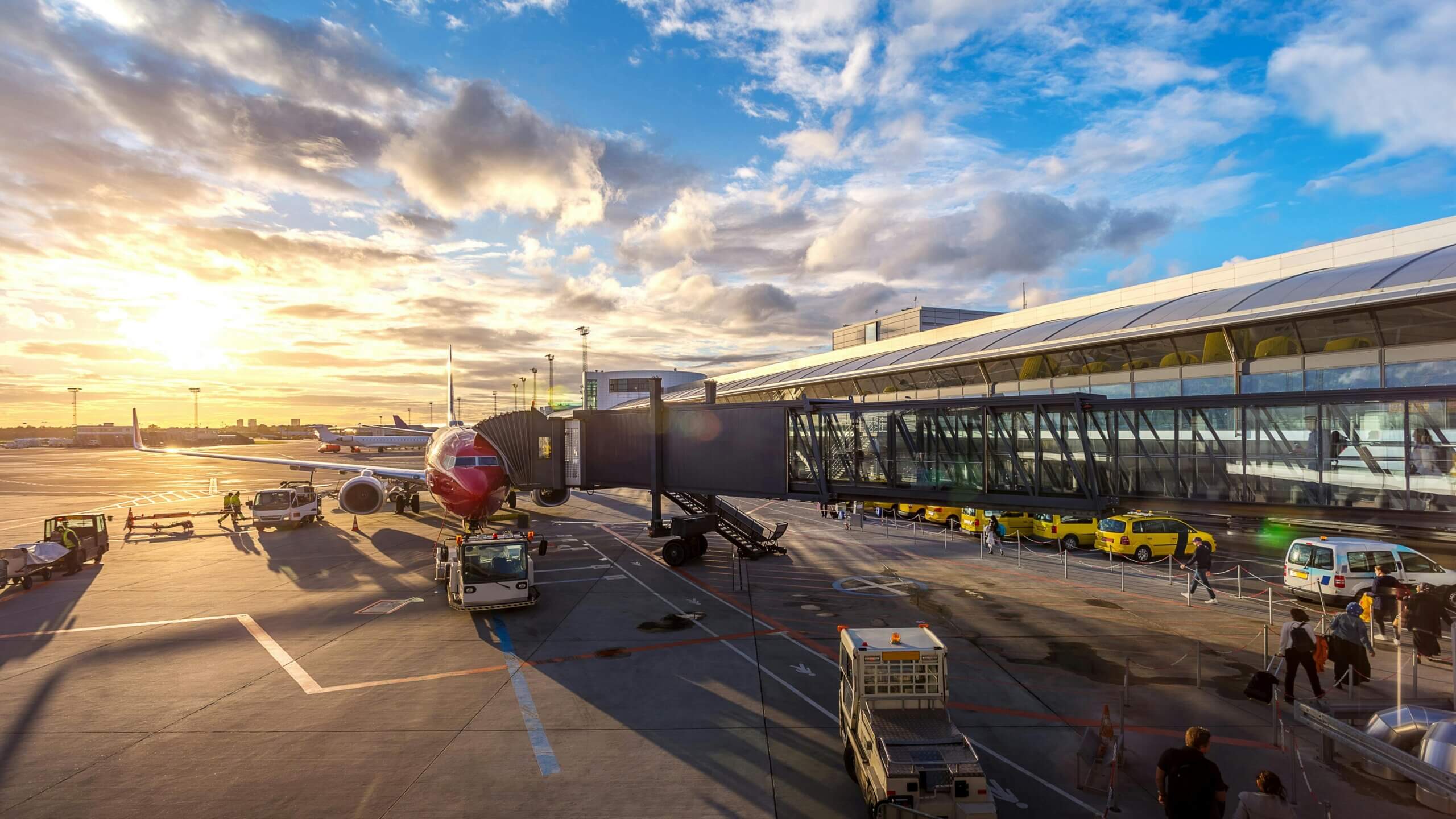 Commercial airplane parked at airport gate with jet bridge and ground service vehicles during sunset