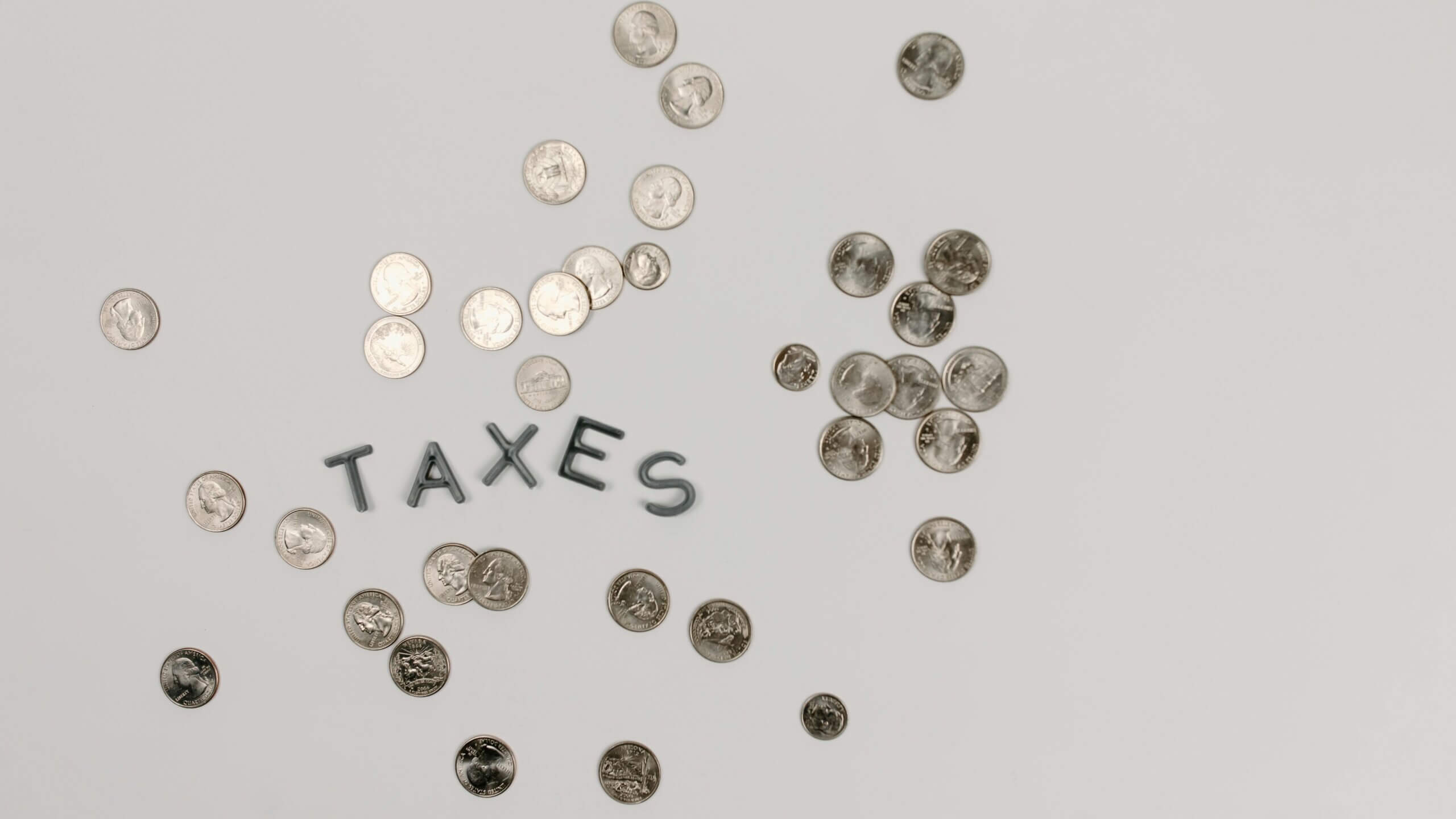 Scattered US coins surrounding the word "TAXES" spelled with black letters on a white surface.
