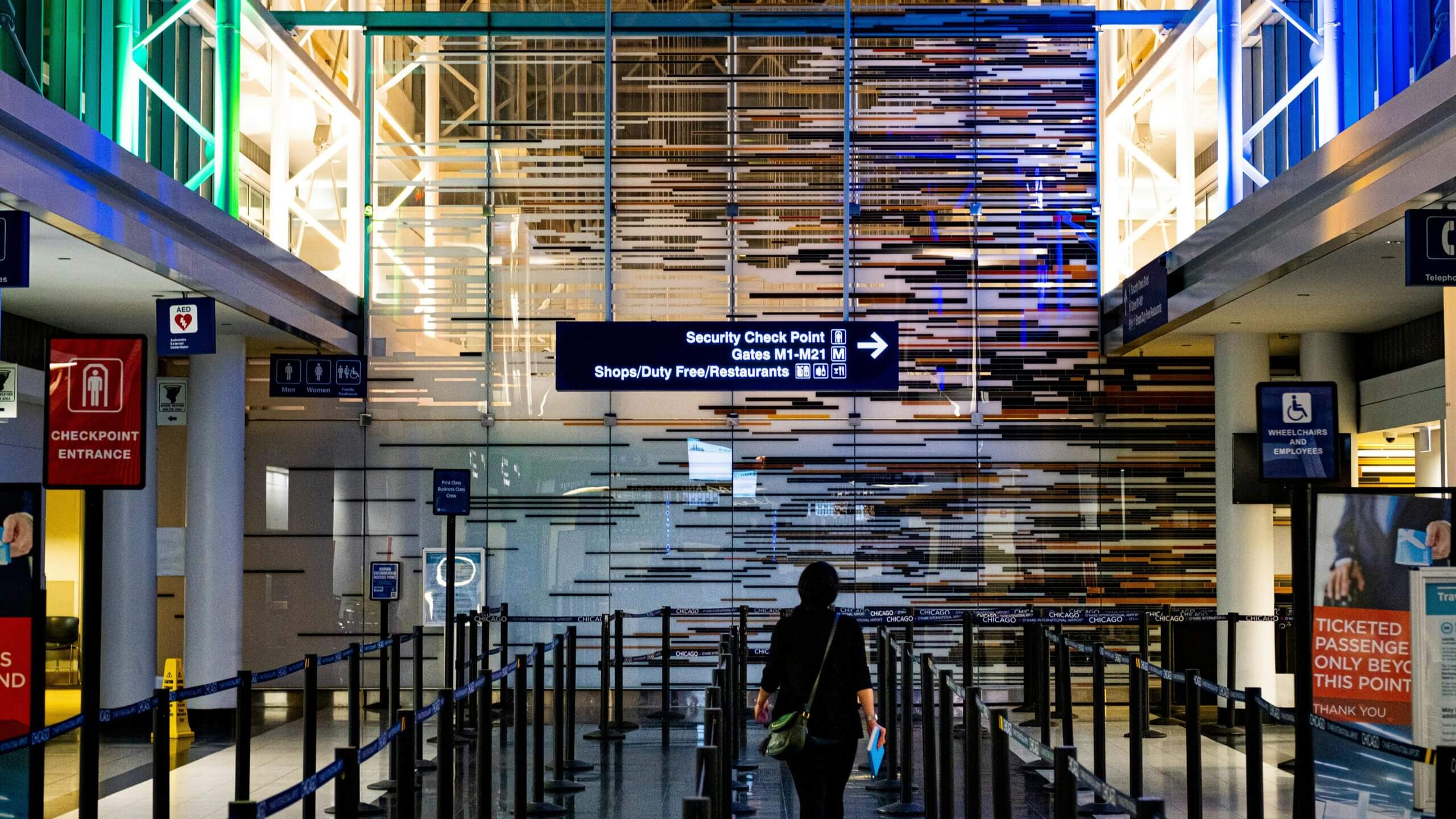 Person walking toward security checkpoint at Chicago O'Hare International Airport with directional signs overhead