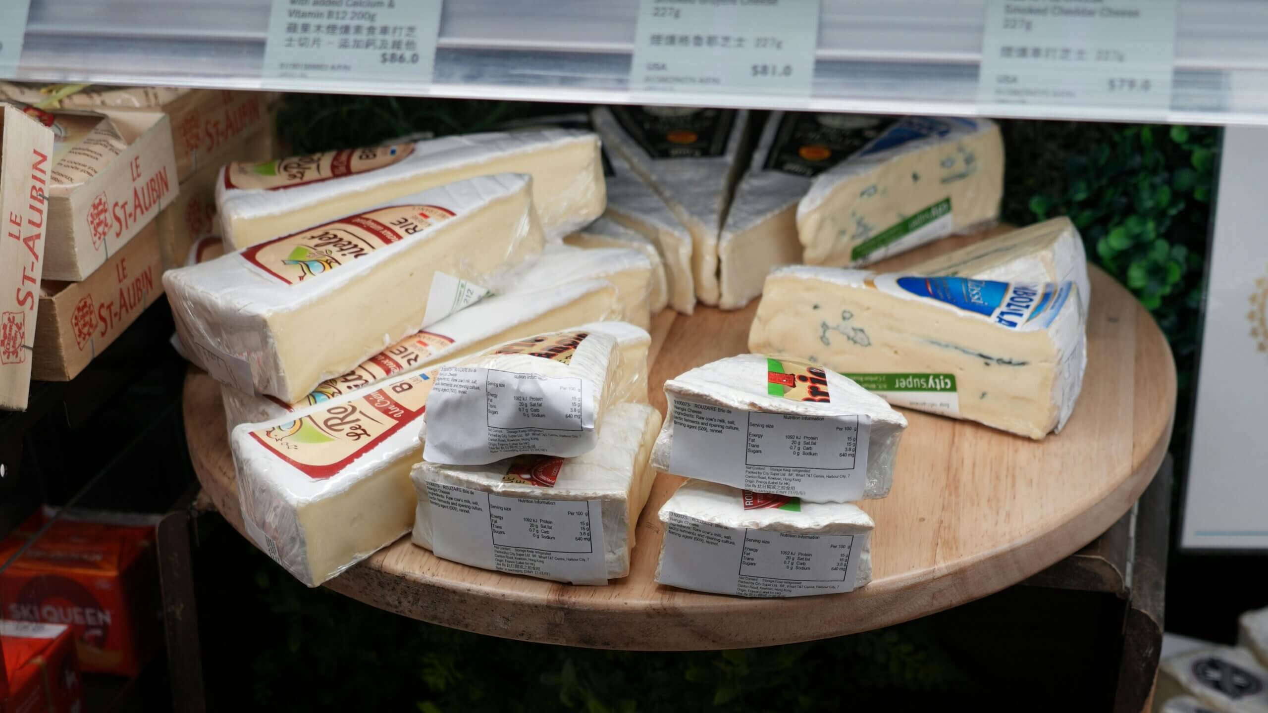 Various wedges of Le St-Aubin and Rouzaire Brie cheeses displayed on a wooden round board
