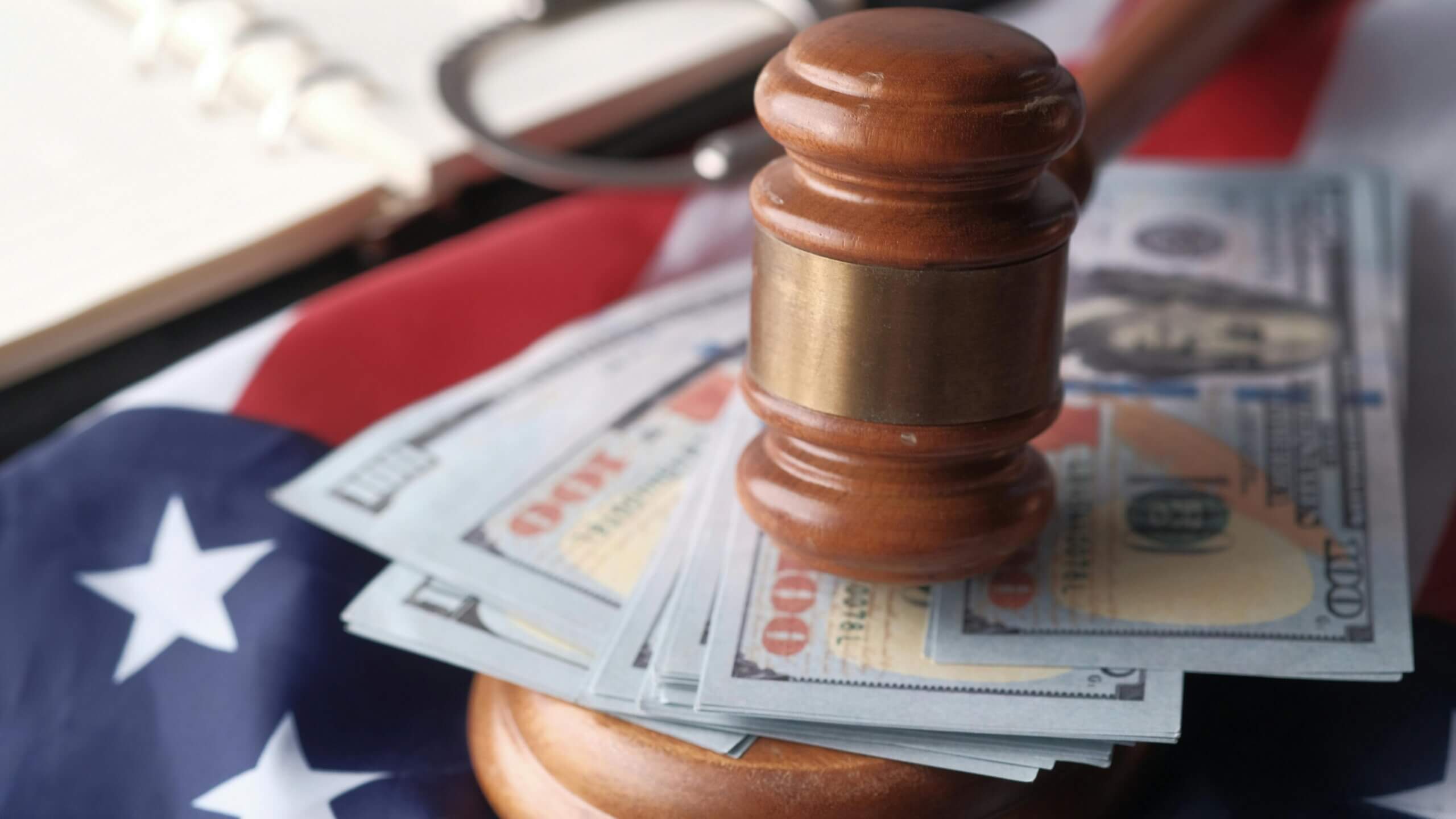 Wooden judge gavel resting on US hundred-dollar bills and an American flag background.