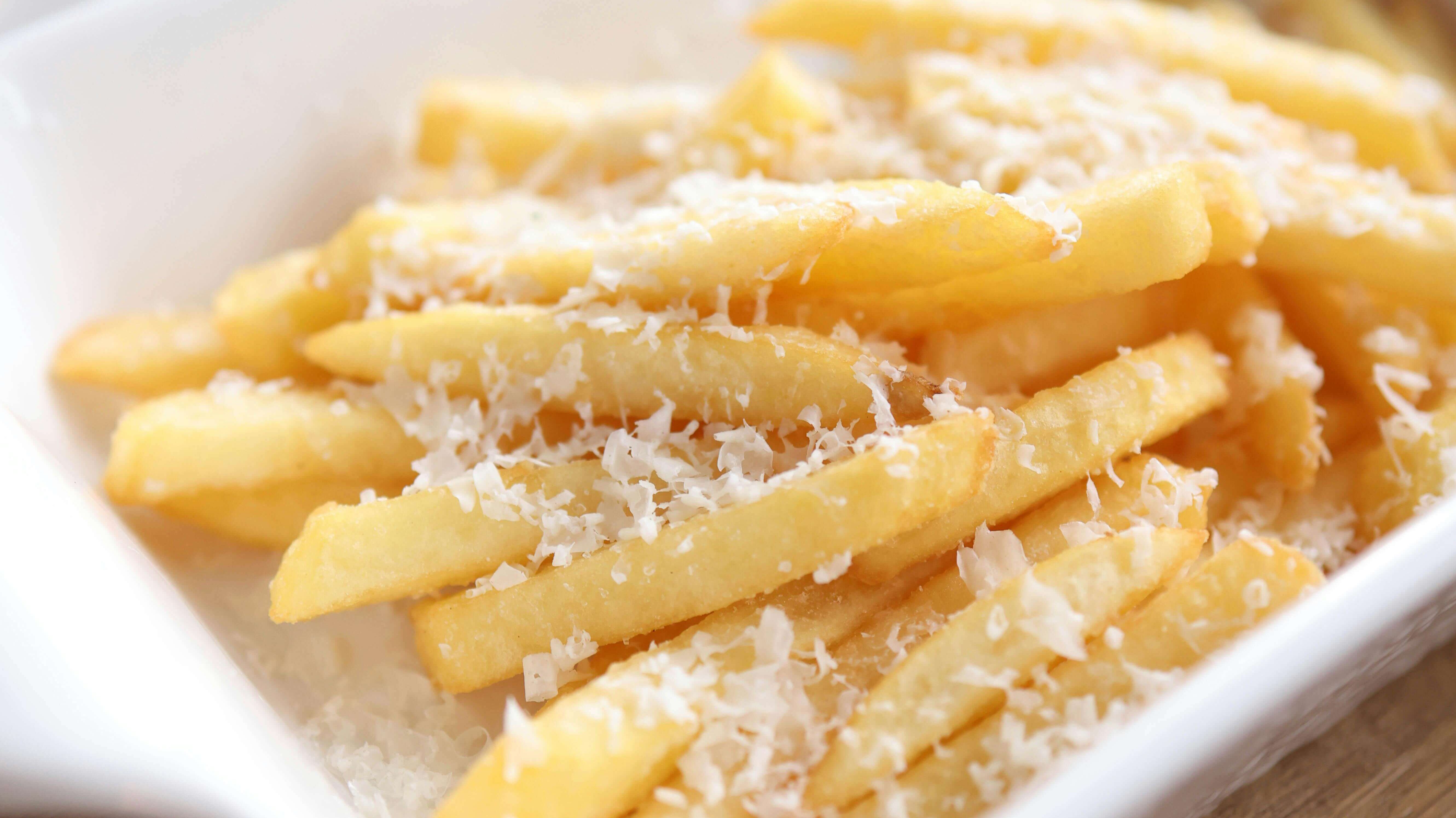 French fries topped with grated Parmesan cheese in a white ceramic dish on a wooden table.