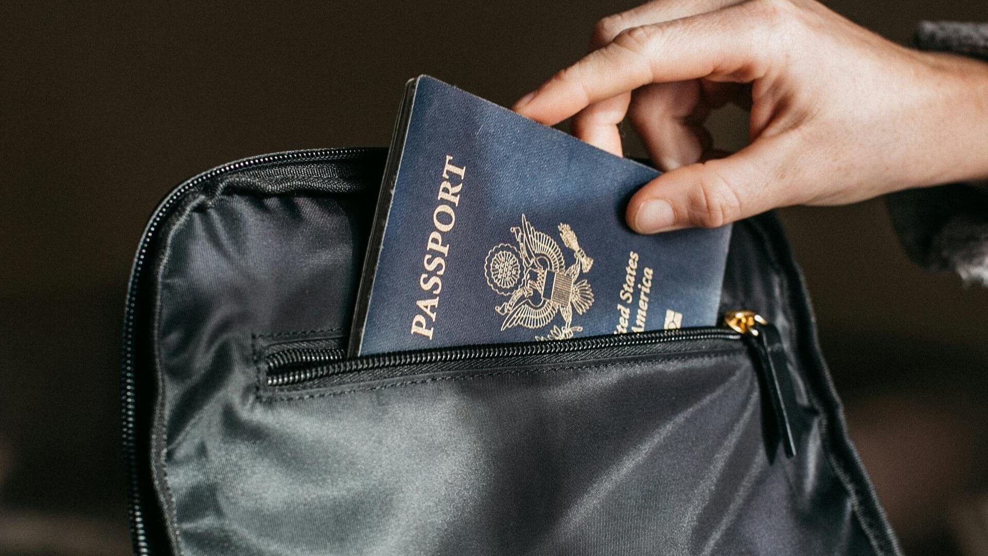Hand placing a United States passport into a black zippered bag pocket.