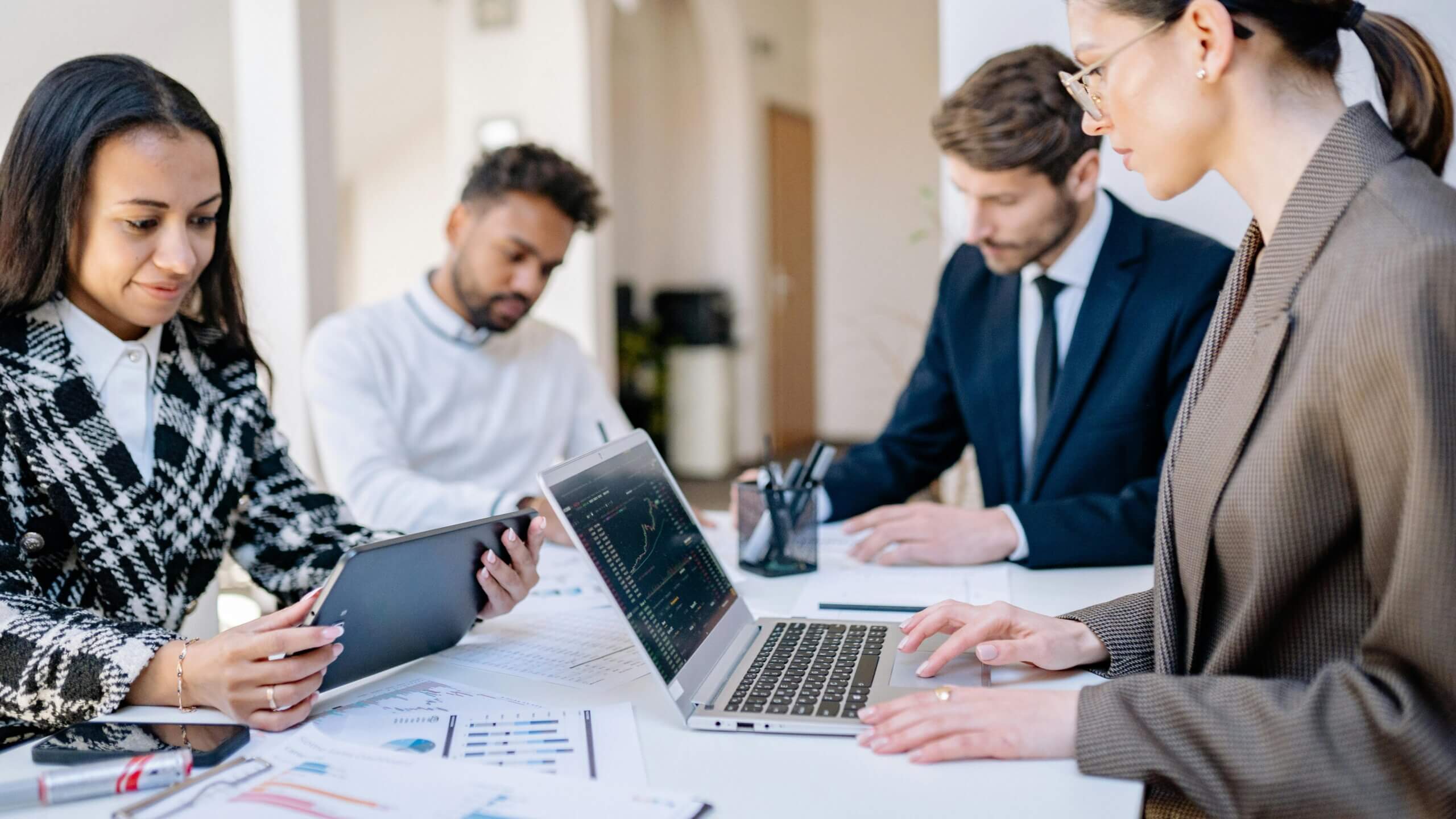Four business professionals analyzing data on a laptop and tablet during a meeting