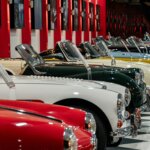 Row of vintage convertible cars in various colors displayed in a museum with checkered floor and red pillars