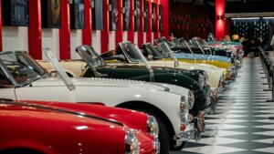 Row of vintage convertible cars in various colors displayed in a museum with checkered floor and red pillars
