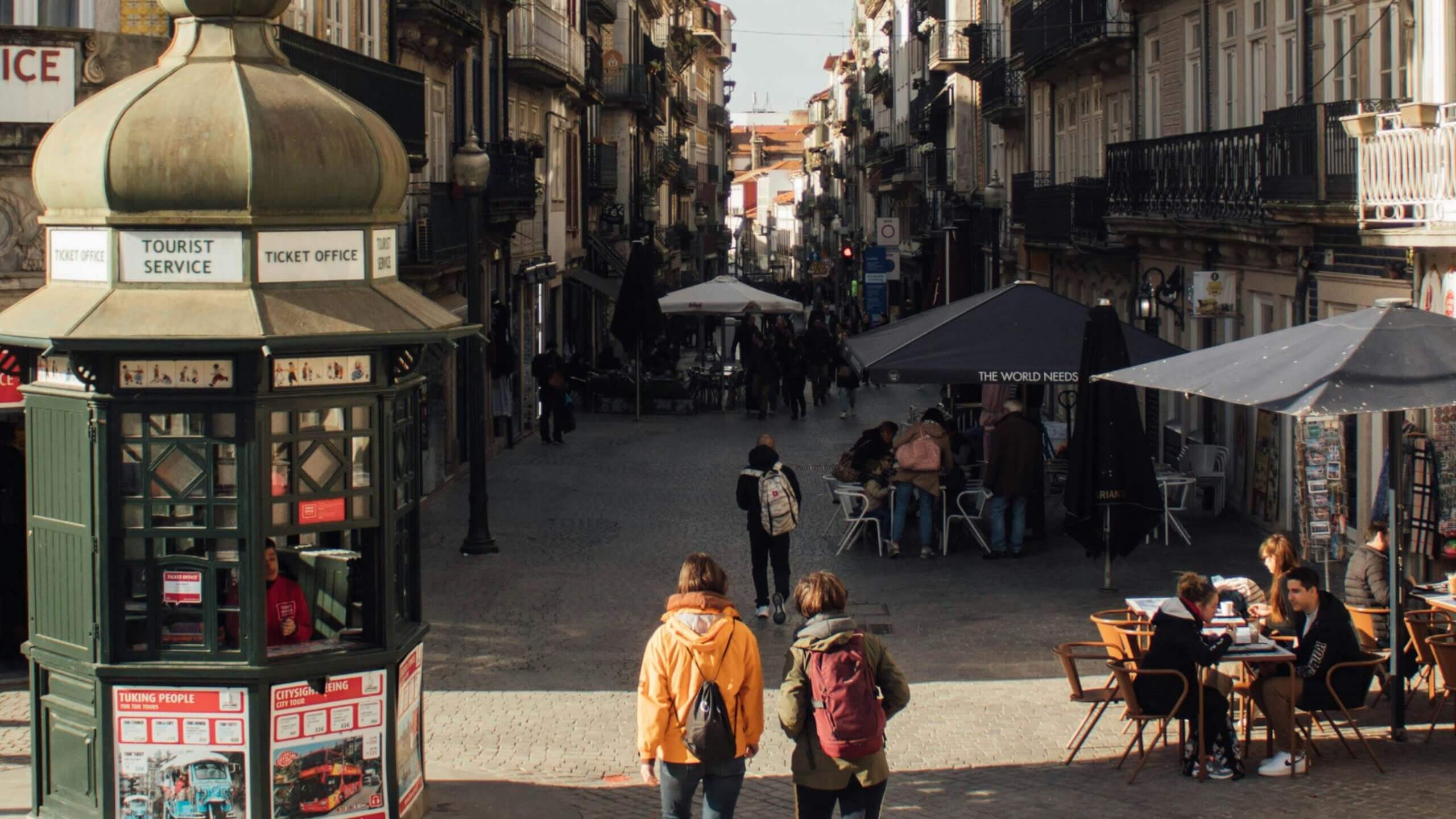 Tourist service ticket office kiosk on a busy European street with people walking and dining outdoors.