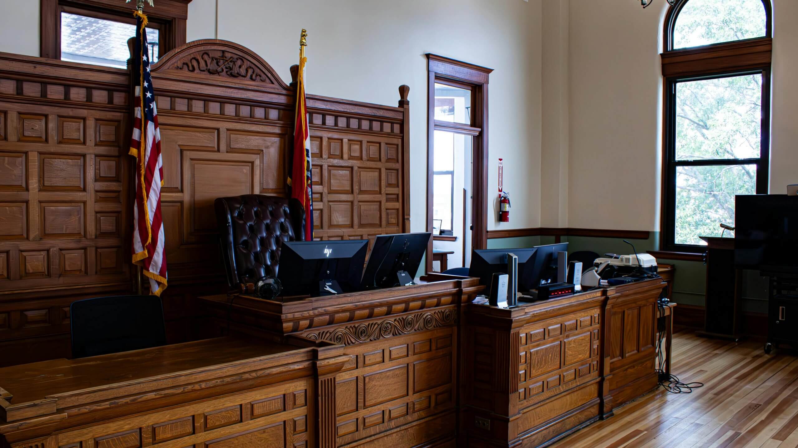 Empty courtroom with wooden judge's bench, American and Missouri state flags, and computer monitors.