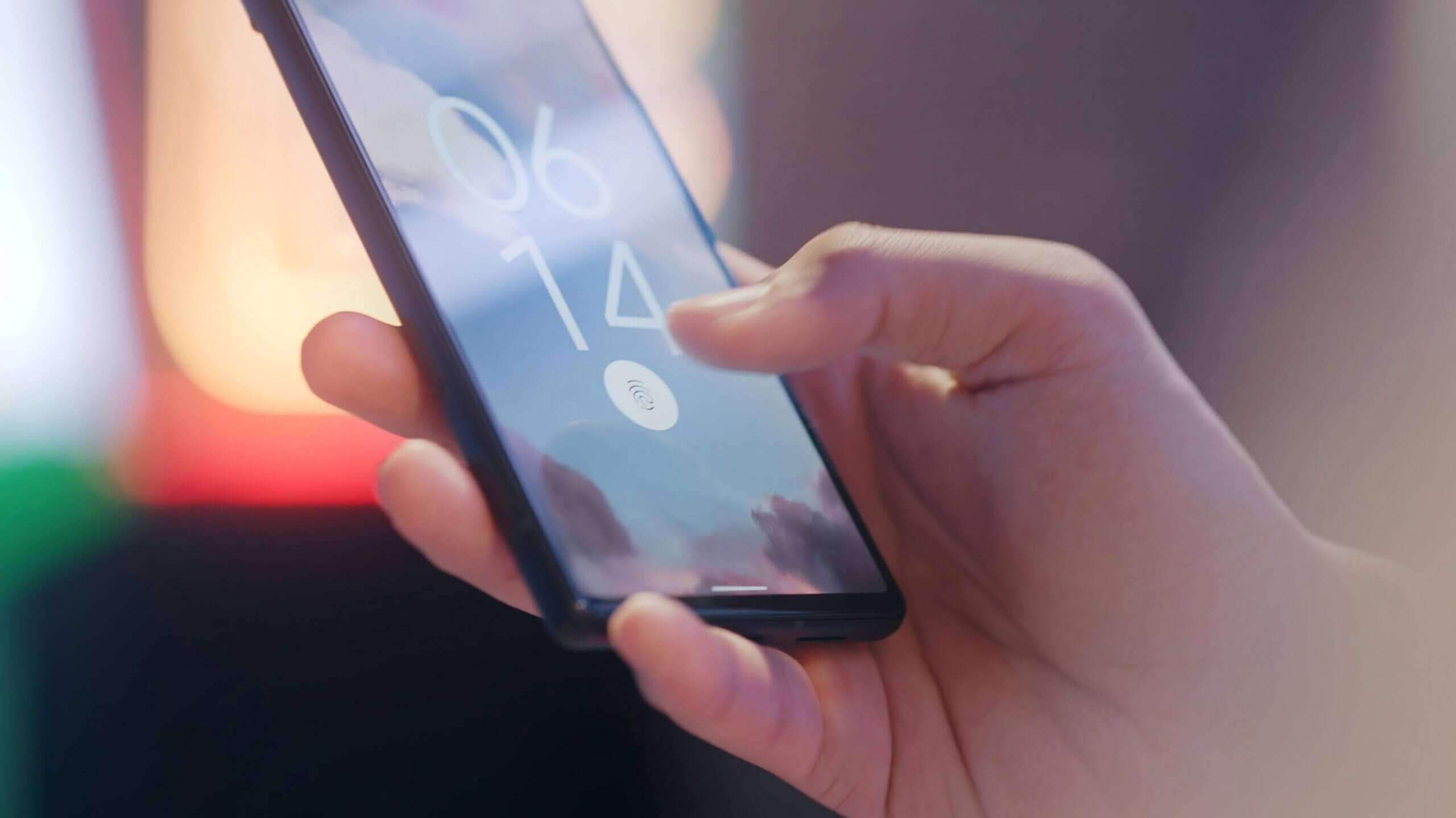 Hand holding a smartphone with a fingerprint icon on the screen showing the time 06:14