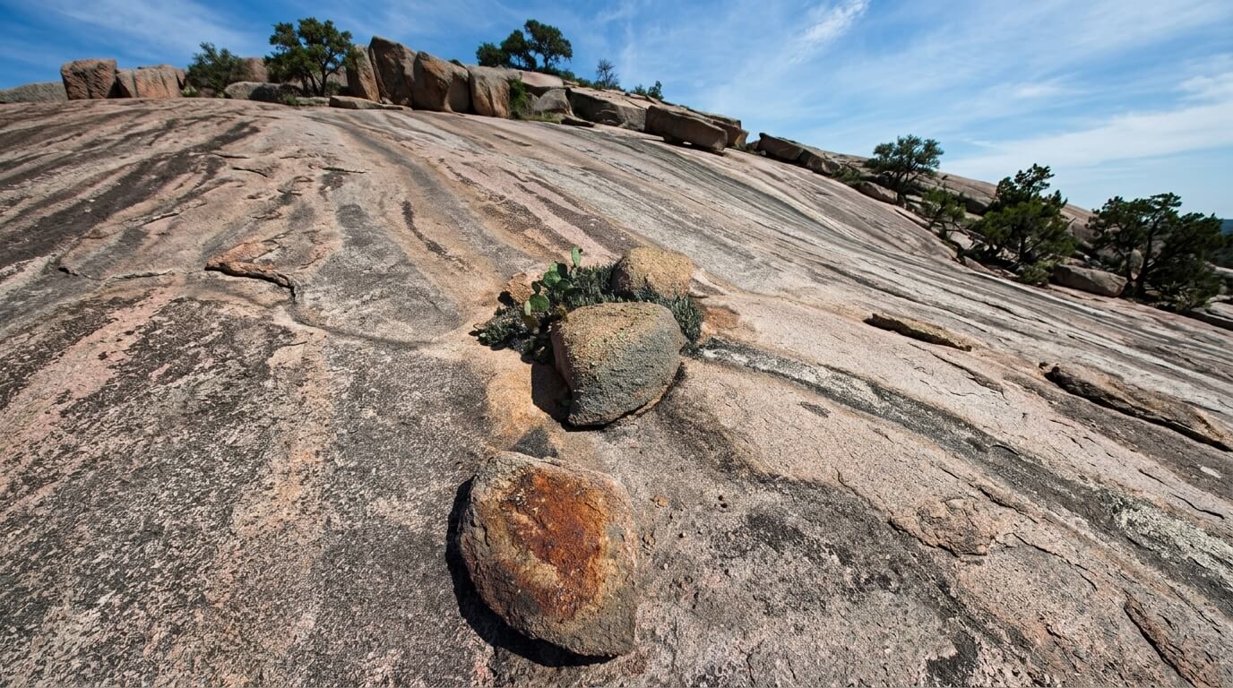 rocky granite slope with scattered boulders and small cactus plants under a blue sky