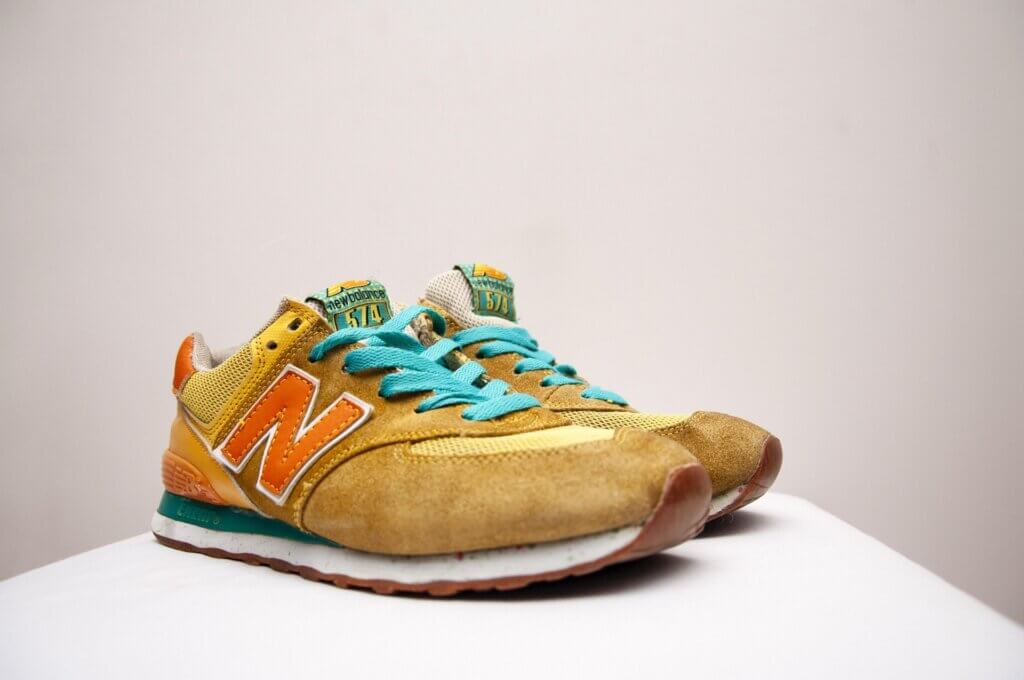 New Balance 574 sneakers in yellow and orange with turquoise laces on a white surface