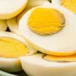 Close-up of halved hard-boiled eggs with firm yolks on a green plate.