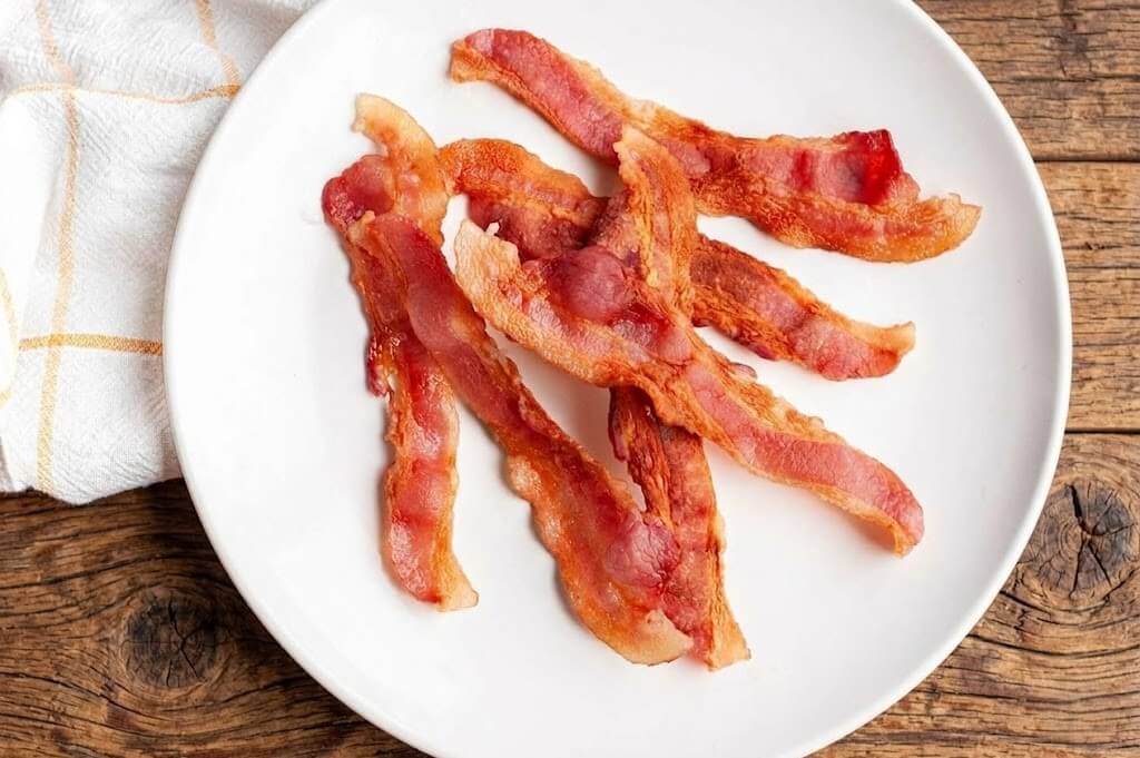 Crispy cooked bacon strips on a white plate with a wooden table background