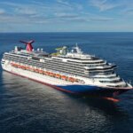 Carnival Splendor cruise ship sailing on calm ocean waters near a distant coastline.