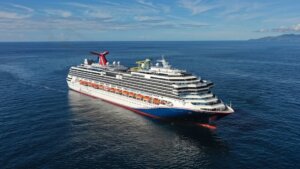 Carnival Splendor cruise ship sailing on calm ocean waters near a distant coastline.