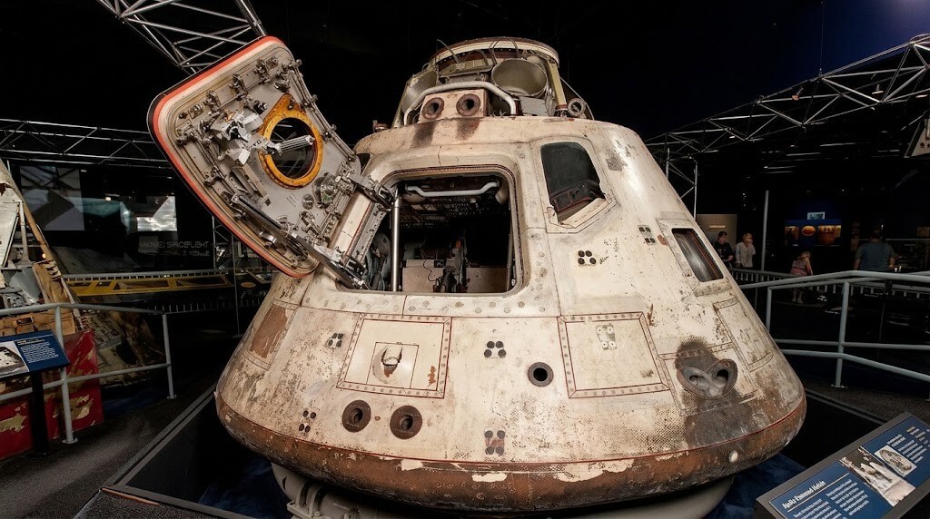 Apollo Command Module with open hatch displayed in a museum exhibit.
