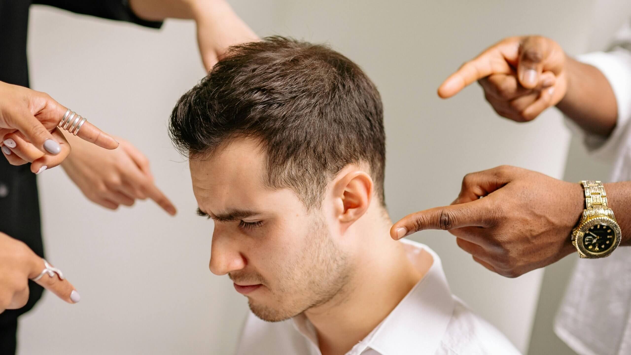 Young man looking down with multiple hands pointing fingers at him from different directions.