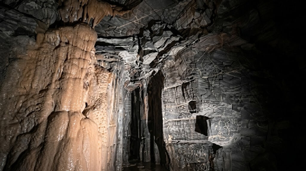 Stalactites and stalagmites inside a dimly lit limestone cave passage.