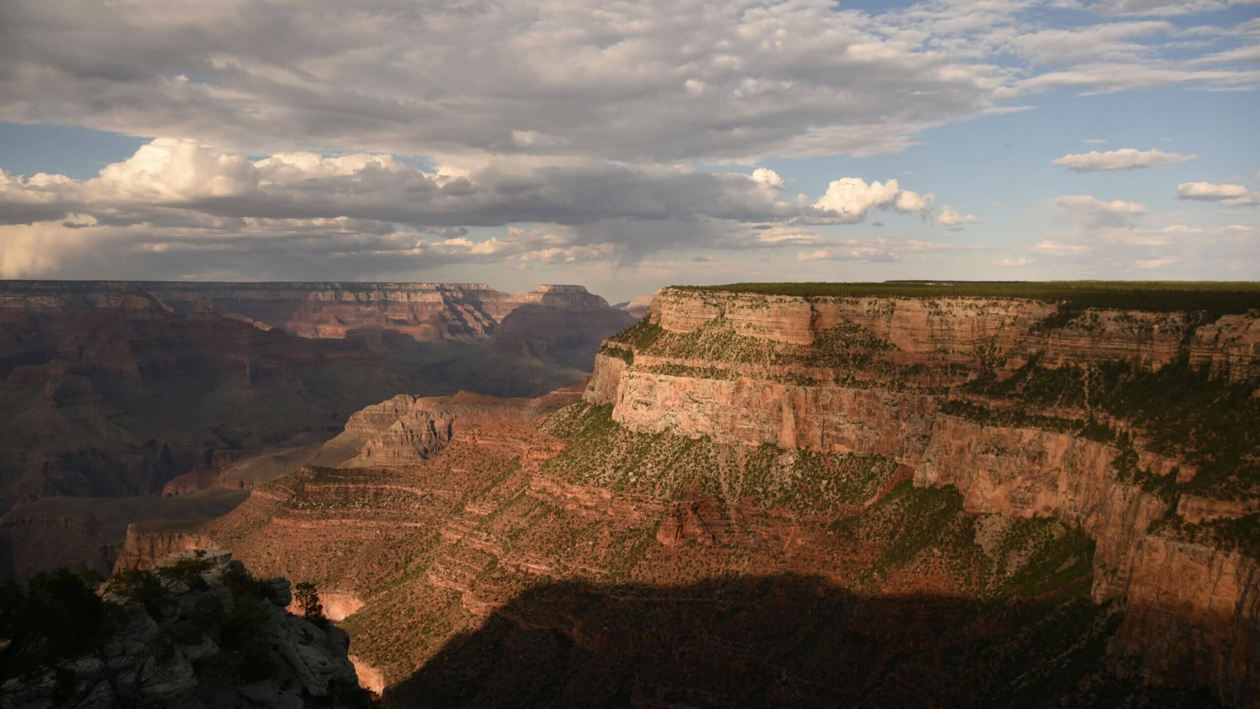 Grand Canyon cliffs with layered rock formations under a partly cloudy sky at sunset