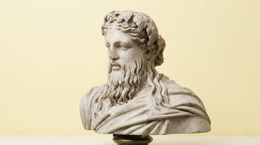 Marble bust of a bearded man with wavy hair and a laurel wreath on a pedestal against a beige background