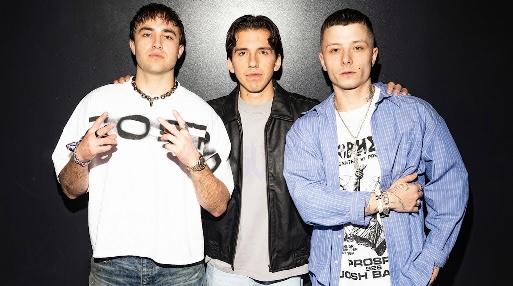 Three young men posing against a black background, one wearing a white T-shirt with "TOFF" text, another in a black leather jacket, and the third in a blue striped shirt.