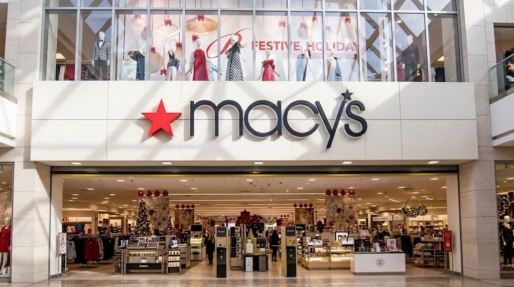 Macy's store entrance with holiday decorations and mannequins dressed in festive clothing above.
