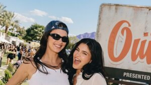 Two smiling women, one wearing a blue Adidas cap and sunglasses, posing outdoors at a sunny event.