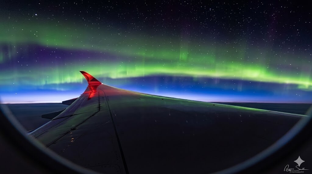 Northern lights visible from airplane window over wing at night.
