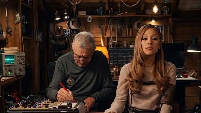 Older man working on electronic equipment while young woman sits beside him in a workshop