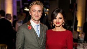 Tom Felton in a gray suit with a poppy pin and Selena Gomez in a red dress at a formal event.
