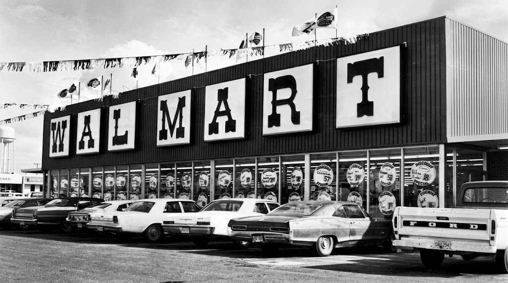 Vintage Walmart storefront with classic cars and a Ford pickup truck parked outside.