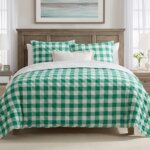 Bed with green and white checkered bedding in a bright bedroom with wooden furniture and white curtains.