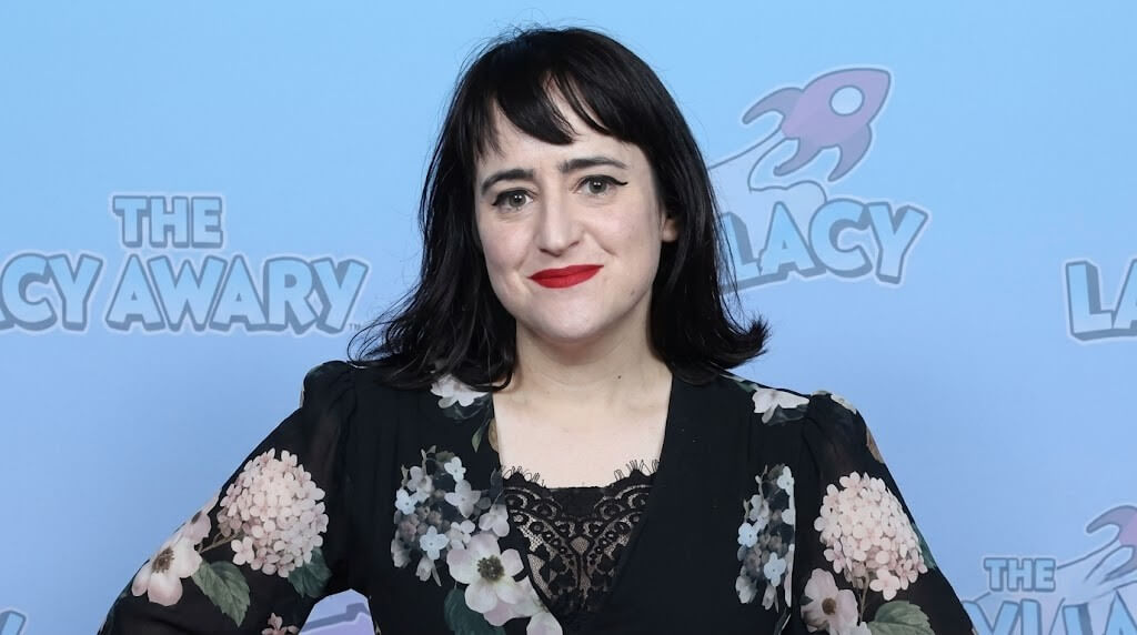 Woman with black hair and red lipstick wearing a black floral dress at The Lacy Awards event backdrop