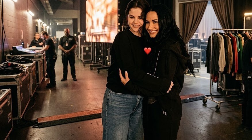 Selena Gomez and Demi Lovato hugging backstage in casual clothing.