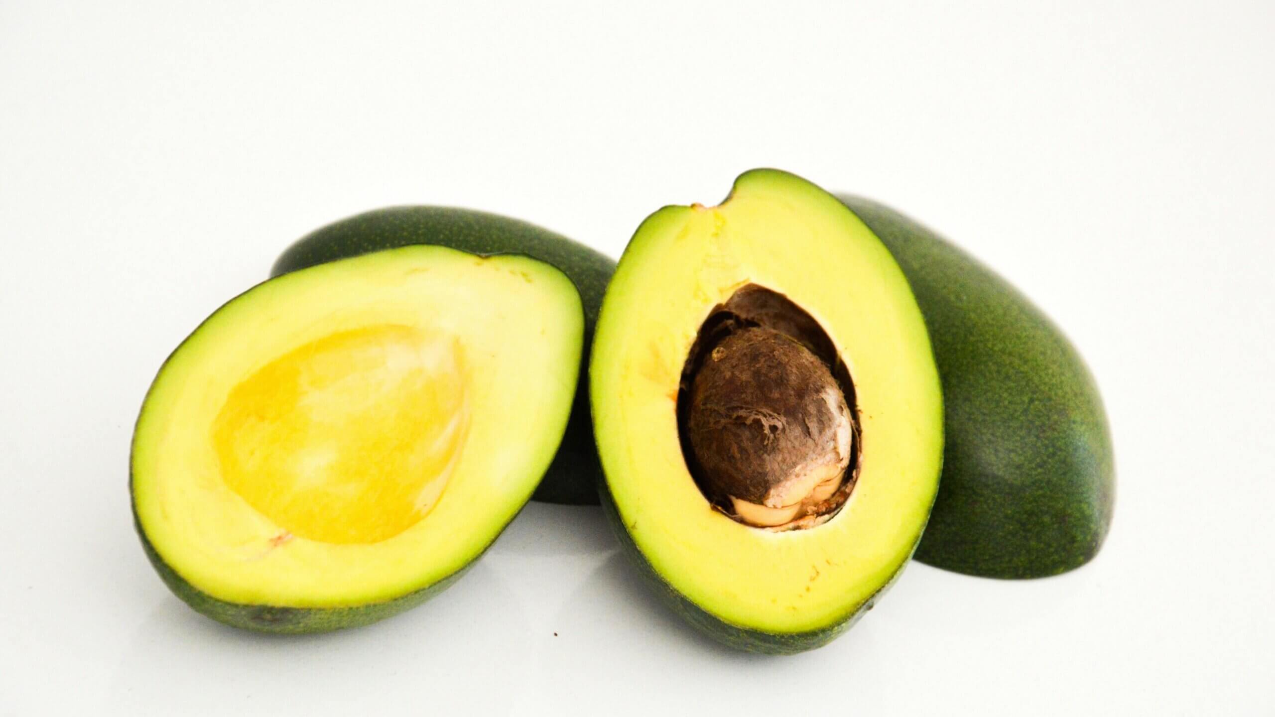 Two halves of a ripe avocado with one half showing the seed on a white background