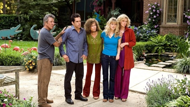Five adults standing closely together in a garden with lawn ornaments and flowers.