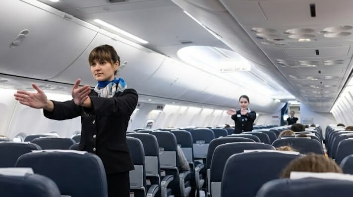 Flight attendants demonstrating safety procedures inside an airplane cabin.