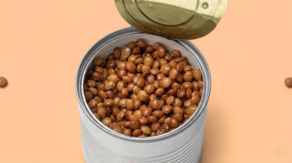 Open tin can filled with cooked brown lentils on a beige background