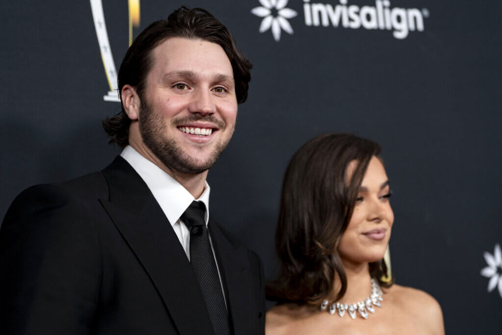 Man in black suit and tie smiling next to woman with shoulder-length hair and diamond necklace at event with Invisalign logo background