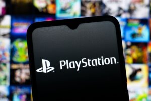 PlayStation logo displayed on a smartphone screen with blurred video game covers in the background.