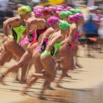 Female swimmers in colorful swim caps and suits sprinting on a beach at a swim race start