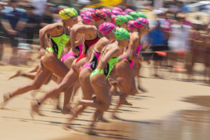 Female swimmers in colorful swim caps and suits sprinting on a beach at a swim race start