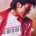 Two men in black suits with red armbands standing on a red carpet in front of a Michael Jackson tribute backdrop