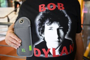 Person wearing a black Bob Dylan t-shirt holding a gray XL camera lens case.