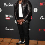 Kevin Hart wearing a black leather jacket and white shirt at Netflix is a Joke Fest event backdrop