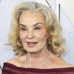 Older woman with blonde hair wearing a burgundy off-shoulder dress and diamond necklace at an event